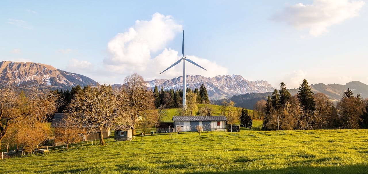 Wind turbine amidst lush country landscape with mountains. A serene depiction of renewable energy in nature.
